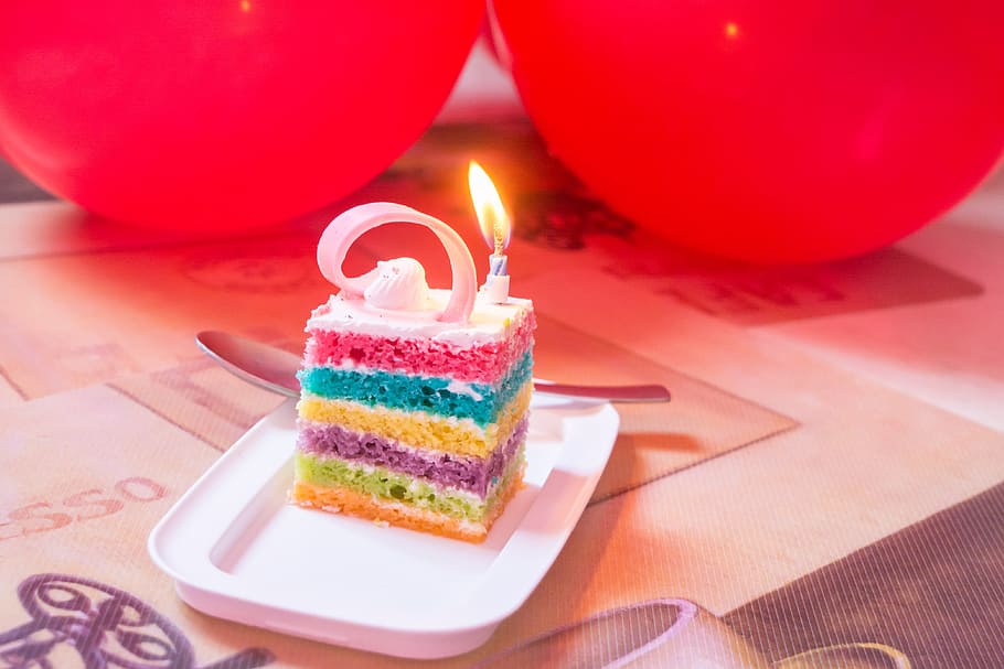 Birthday cake with single candle and balloons in background